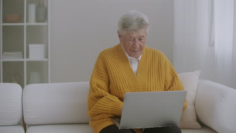 Senior-woman-with-gray-hair-make-video-call-using-laptop-at-home.-Elderly-woman-having-a-video-call-with-family-smiling-and-waving.-COVID-19-Stay-connected.-Online-chatting-with-friends